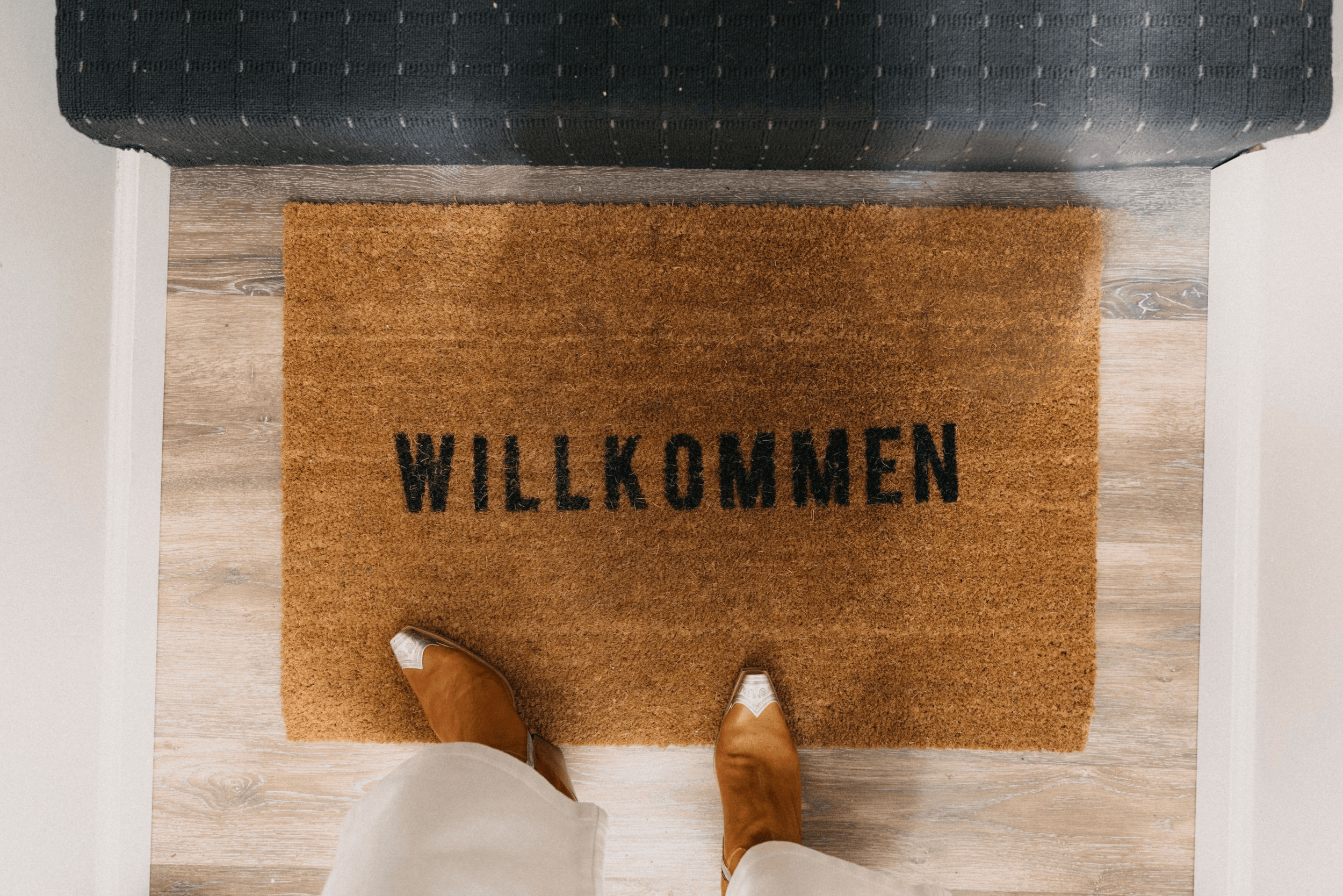 A welcome mat with the word "WILLKOMMEN" and a perspective view of someone's feet.