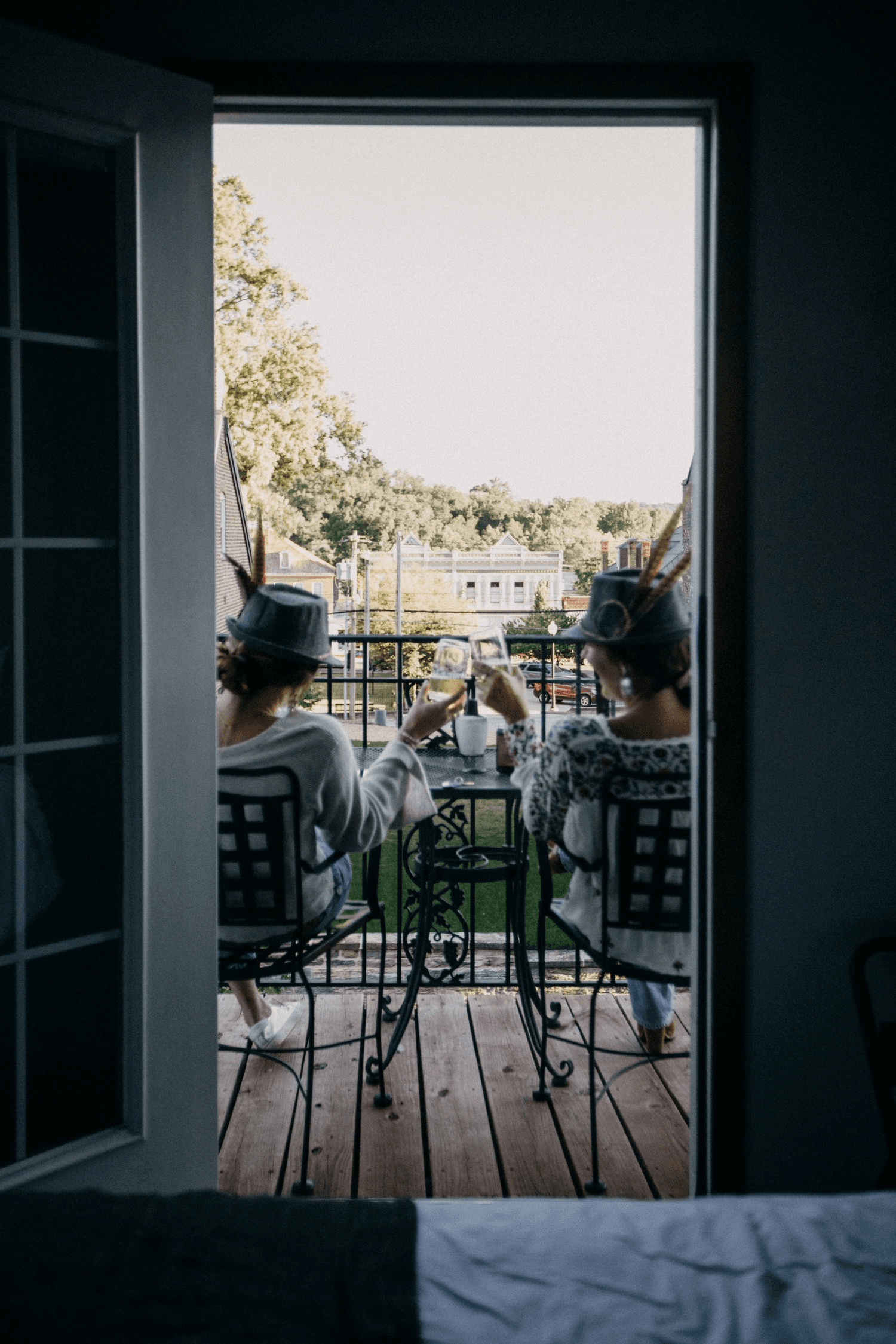Two people toast with drinks while seated on a balcony overlooking a scenic view.
